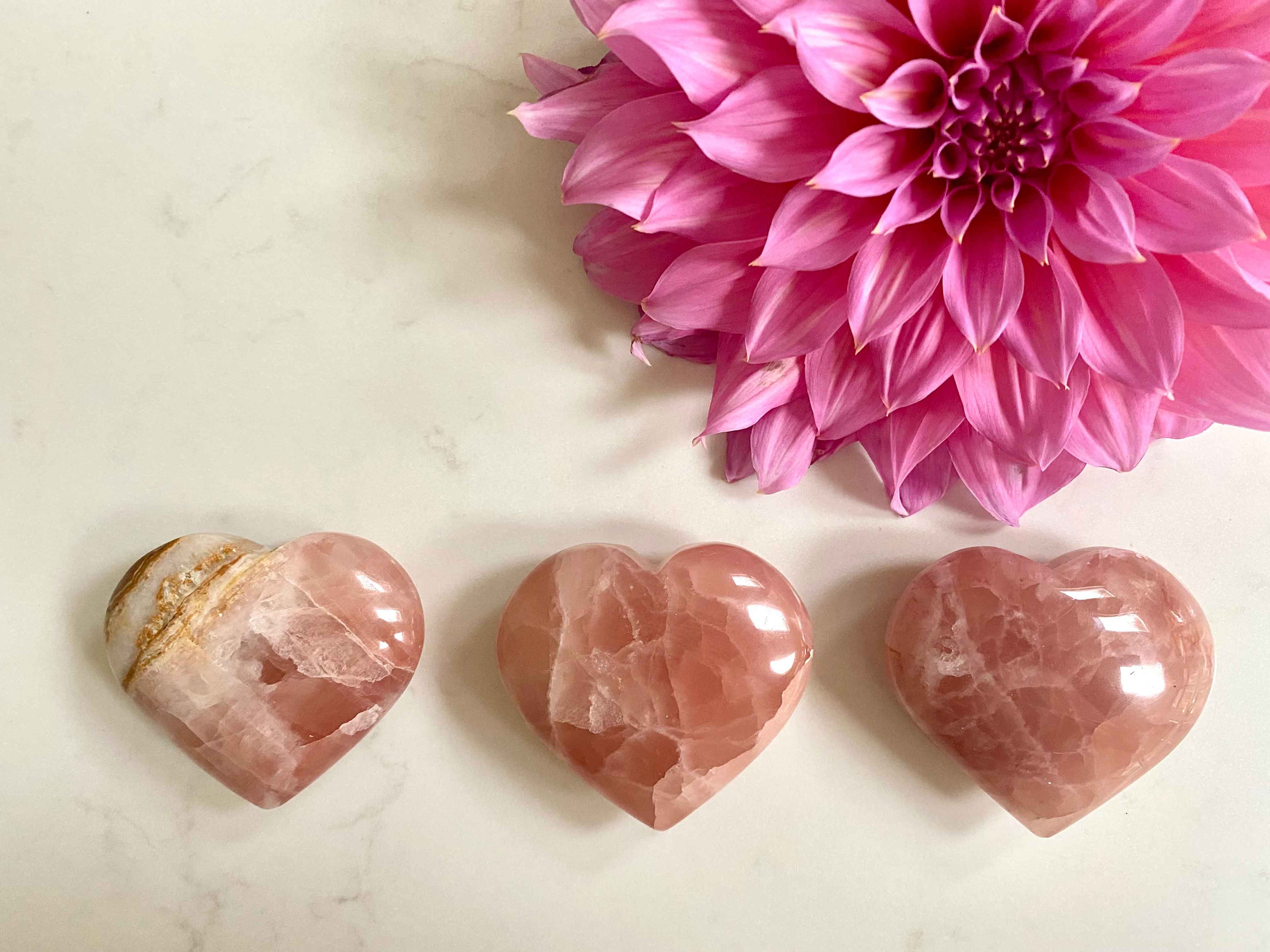 3 Crystal hearts on a table with a large pink flower in the top corner